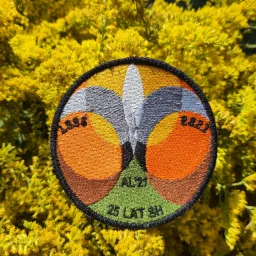 Okrągła, haftowana naszywka z datami 1998 i 2023 oraz napisem '25 LAT SH' na tle żółtych kwiatów Solidago.