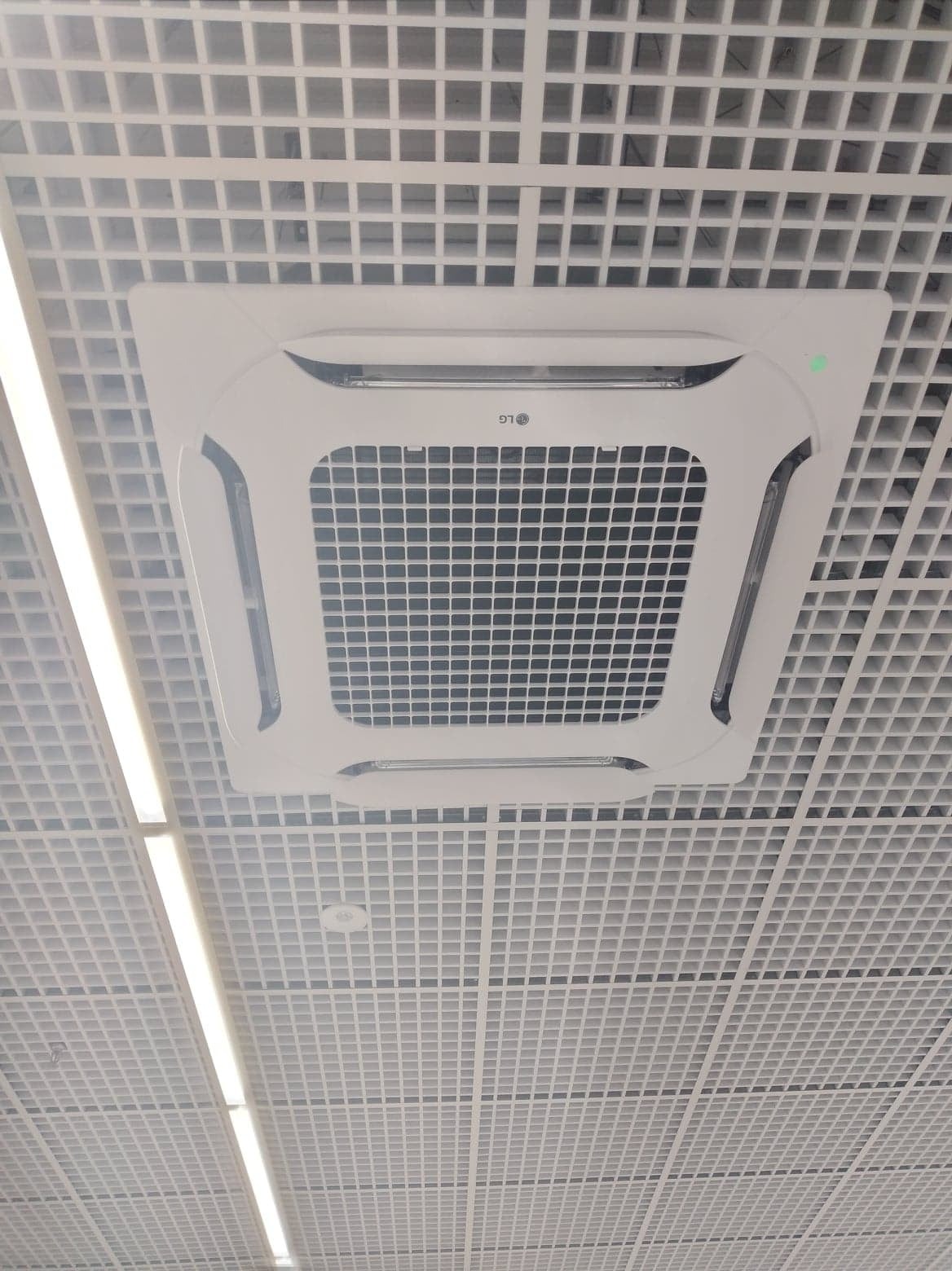 Kasetonowa jednostka klimatyzacyjna LG zamontowana w suficie podwieszanym, widoczna zielona dioda sygnalizacyjna.