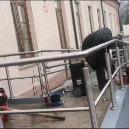 MSC GROUP SP. Z O. O. - Montaż balustrady przy wejściu do budynku szpitala w Legionowie. Trzech monterów przy pracy, widoczne narzędzia i walizki narzędziowe.