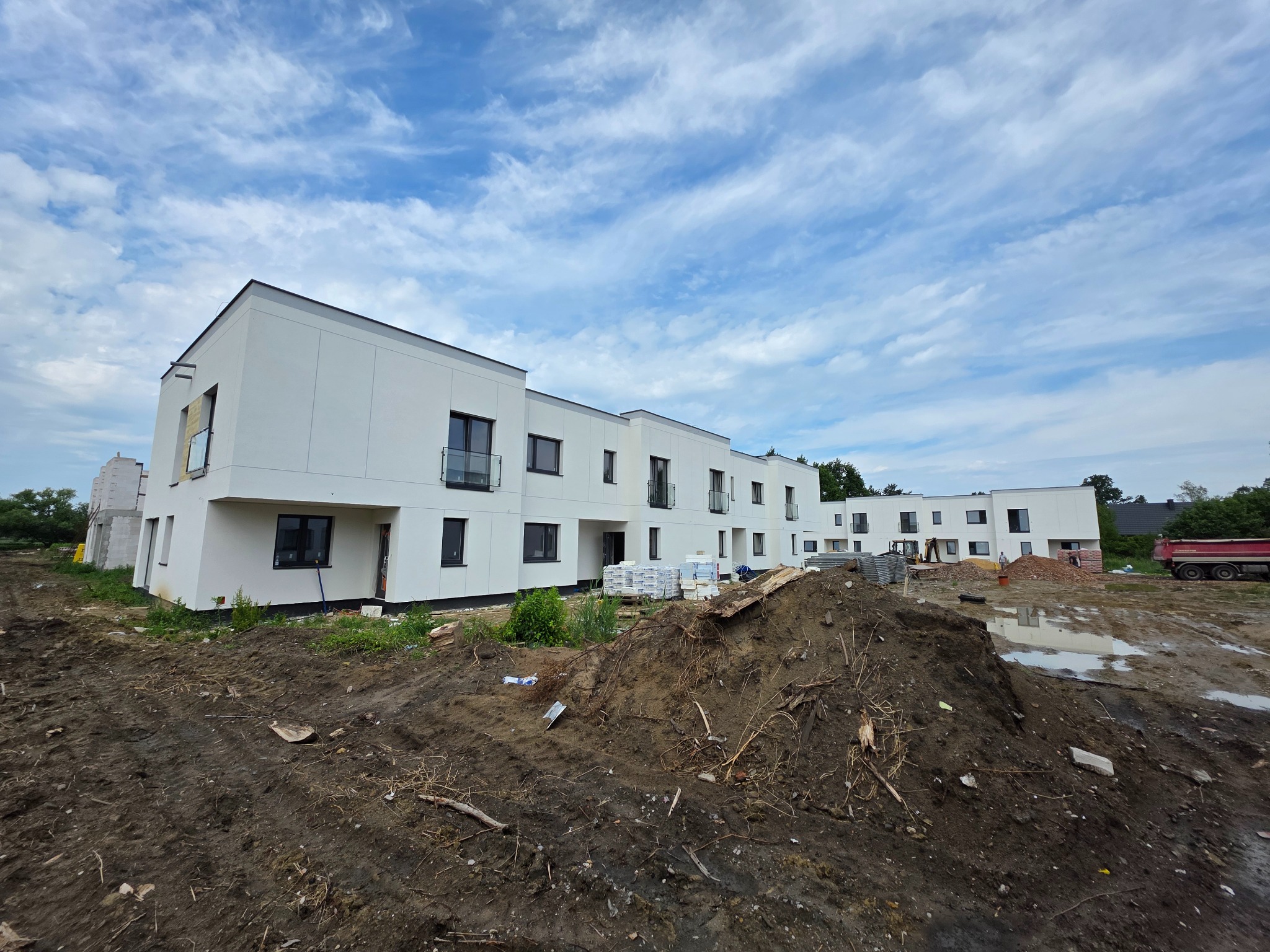 Nowoczesne, białe budynki szeregowe w Halinowie, z czarnymi oknami i szklanymi balustradami, w trakcie budowy, widok z perspektywy ziemi.