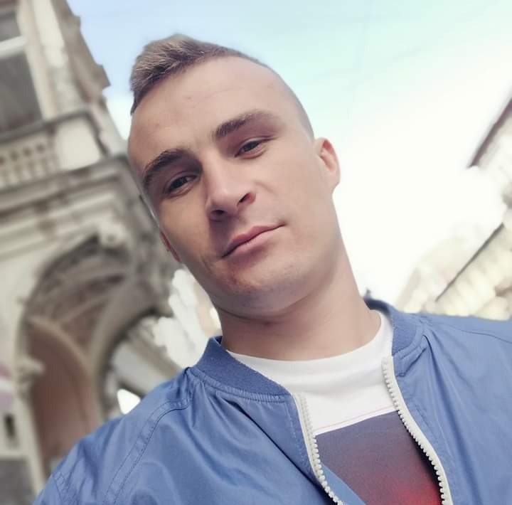 Selfie mężczyzny w niebieskiej kurtce na tle zabytkowej architektury z łukami.