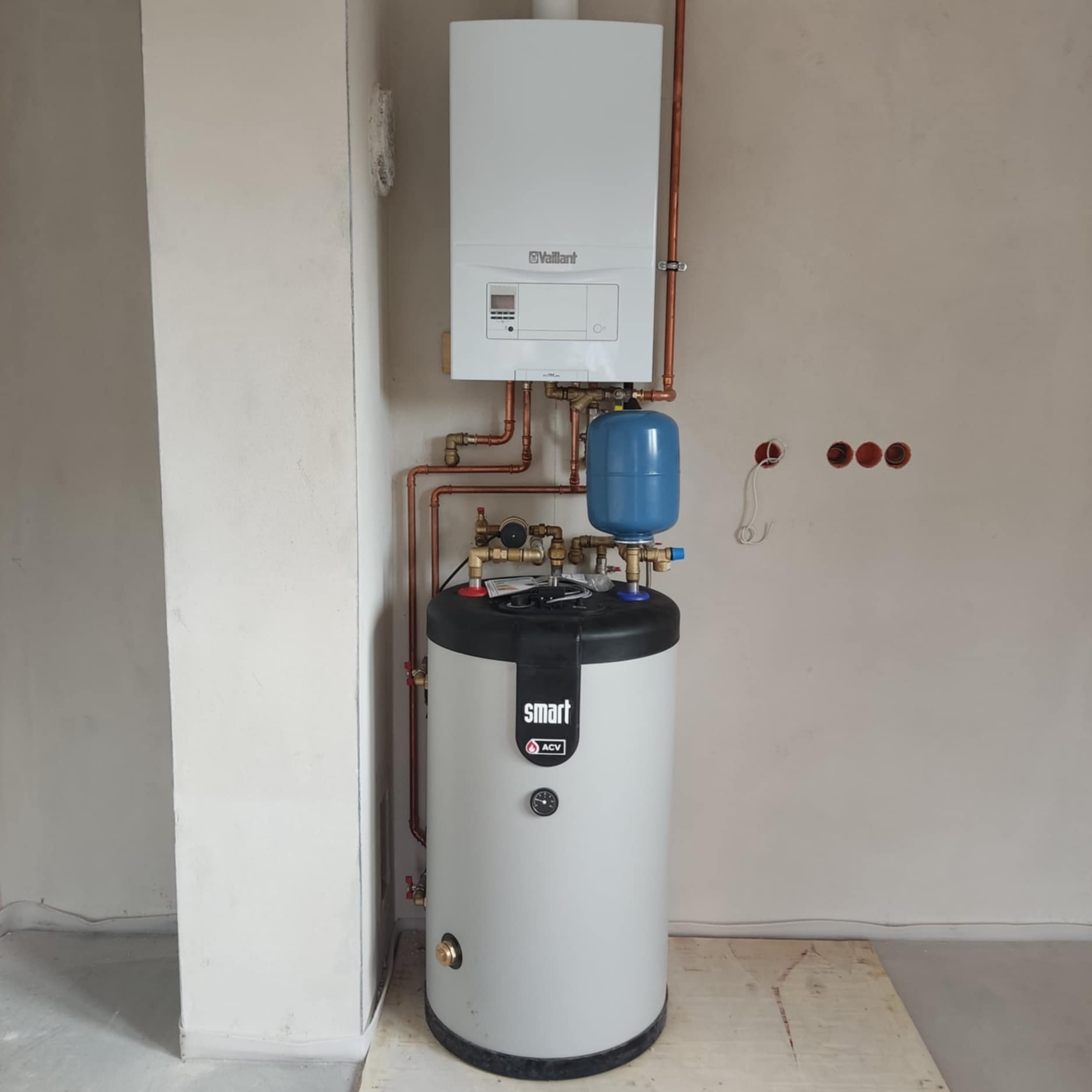 Bojler ACV Smart z osprzętem i piecem Vaillant zamontowany na tle surowych ścian w Blazowej, instalacja z miedzianych rur.