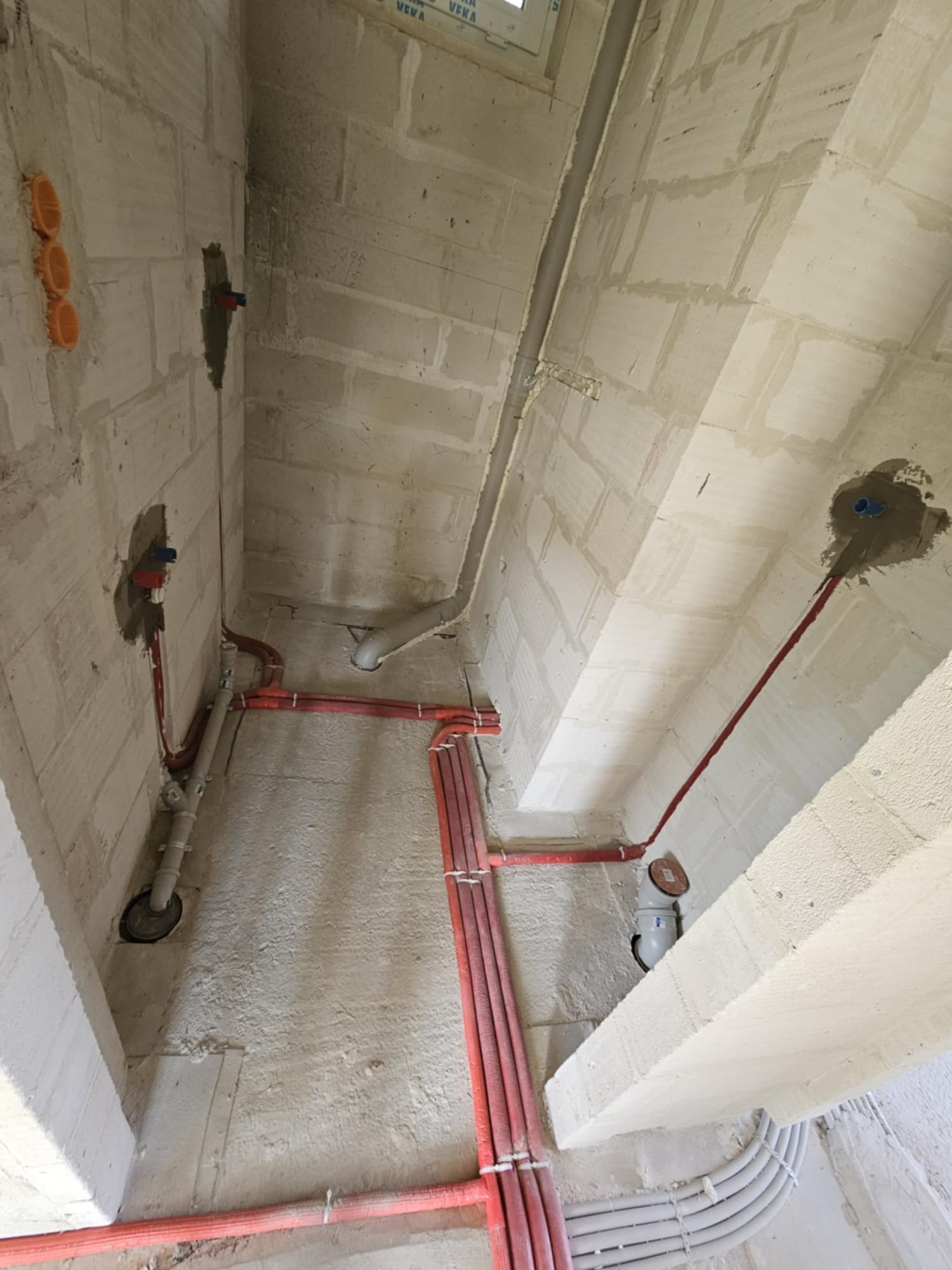 Wewnętrzne instalacje wodno-kanalizacyjne i elektryczne w surowym budynku z betonu komórkowego, widoczne rury w kolorze czerwonym i szarym, kable w peszlach oraz puszki instalacyjne.
