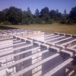 Widok z góry na konstrukcję stropu Teriva z widocznymi belkami i pustakami, przygotowaną do zalania betonem na tle zieleni drzew i łąki.