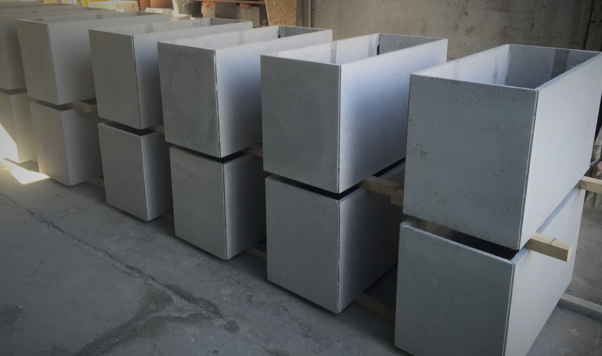 Rząd ułożonych jeden na drugim, surowych, betonowych donic w kształcie prostopadłościanów, oddzielonych drewnianymi listwami, w szarej hali produkcyjnej.