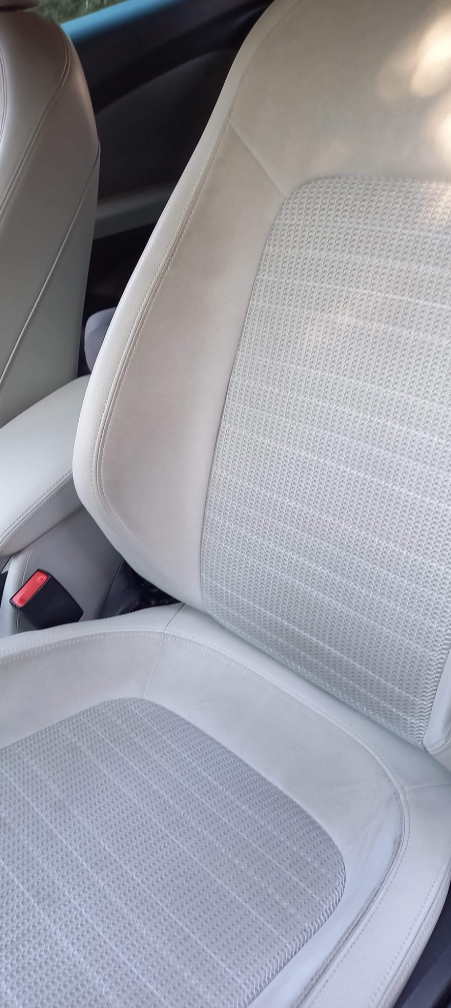 Jasnoszare, tekstylne i skórzane siedzenie samochodowe z widocznym pasem bezpieczeństwa i podłokietnikiem.