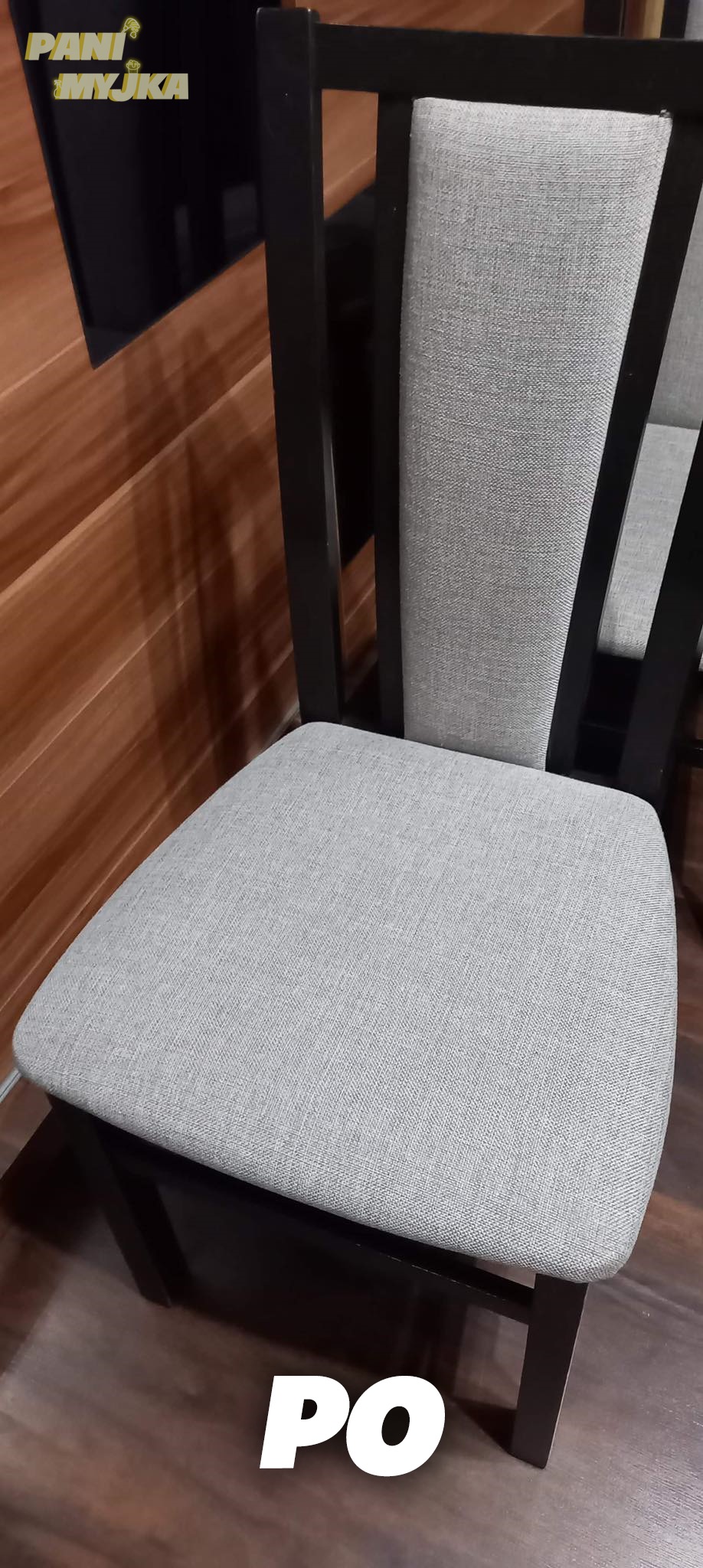 Krzesło z szarą tapicerką i ciemnymi nogami na tle drewnianej ściany i podłogi, widoczny napis 'PO' na dole zdjęcia.