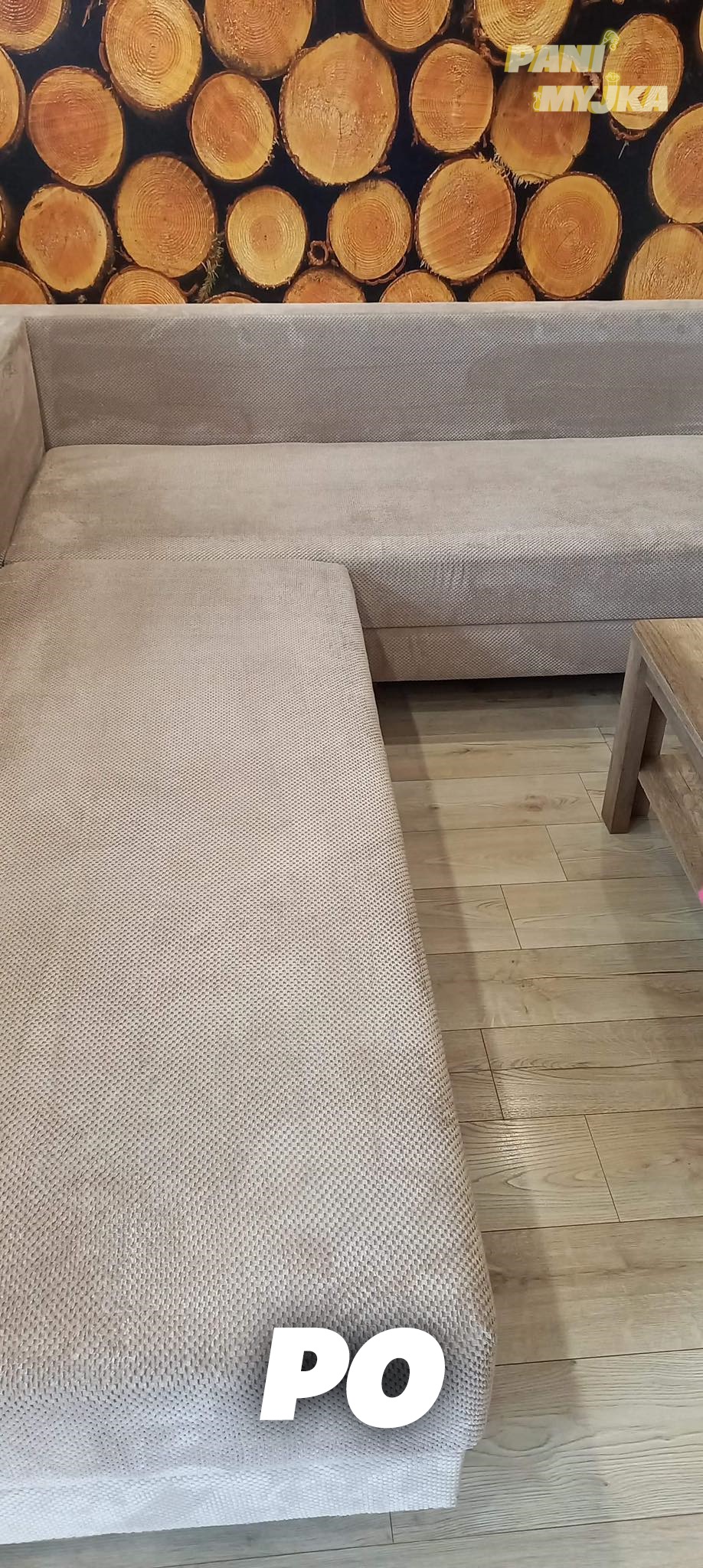 Jasny narożnik z tkaniny o wyraźnej fakturze, na drewnianej podłodze, z tapetą imitującą drewno w tle, z widocznym napisem 'PO' na dole zdjęcia.