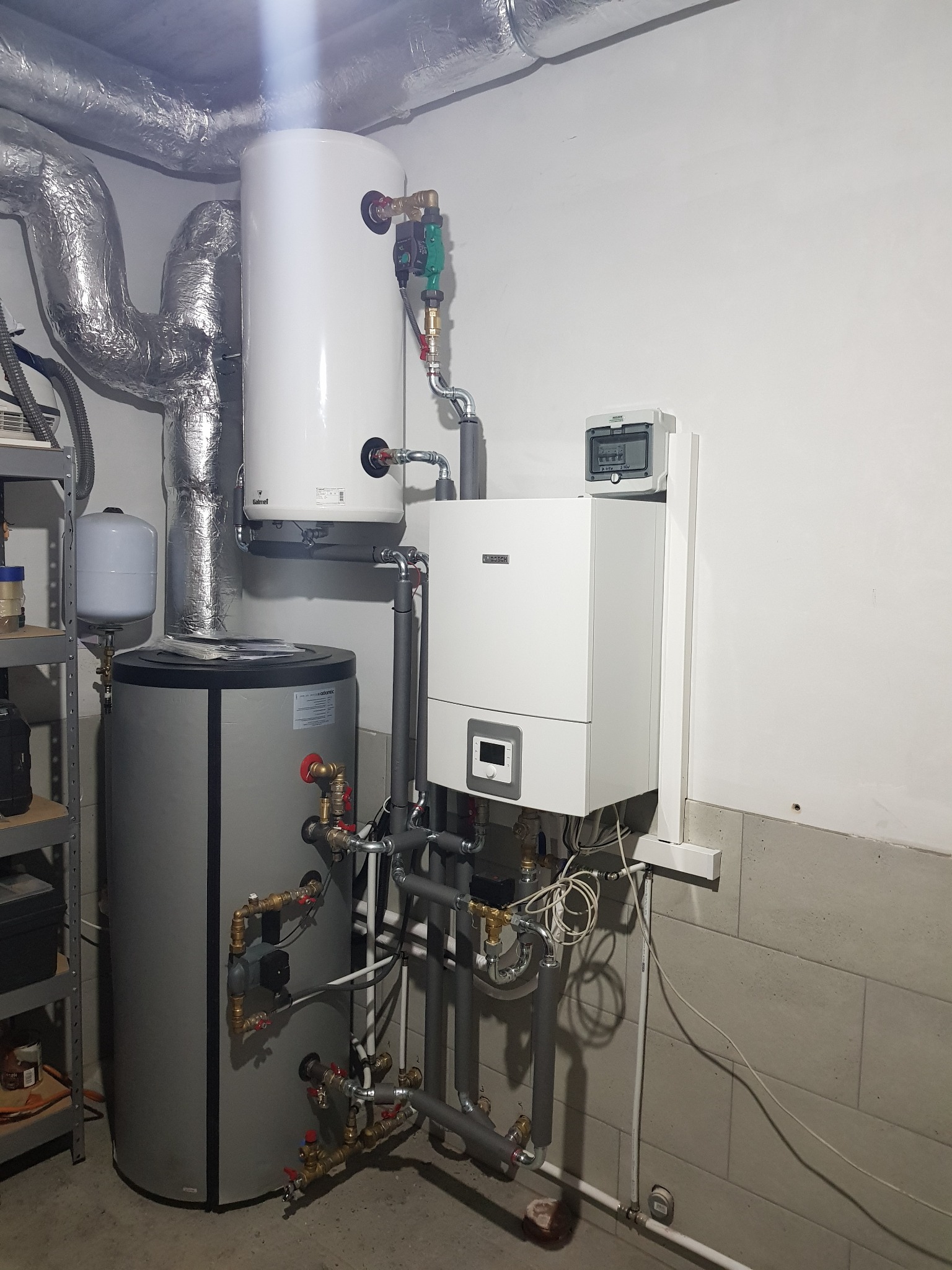 Nowoczesny, biały piec gazowy Bosch z szarym zbiornikiem na wodę Atlantic. Widoczne rury, zawory i przewody. Elementy instalacji grzewczej w kotłowni.