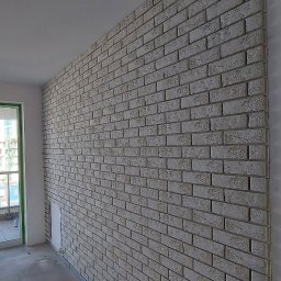 Pan Łazienka - Ściana wyłożona dekoracyjną cegłą w odcieniach szarości, widok na balkon z widokiem na miasto, surowe wykończenie wnętrza.