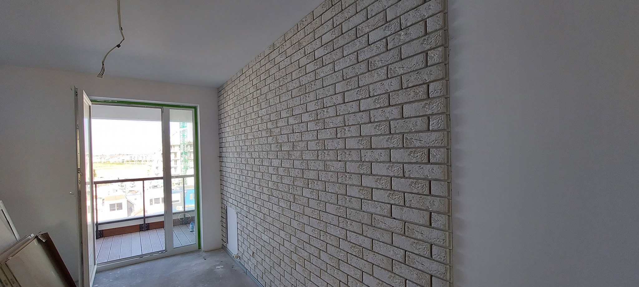 Ściana wyłożona dekoracyjną cegłą w odcieniach szarości, widok na balkon z widokiem na miasto, surowe wykończenie wnętrza.