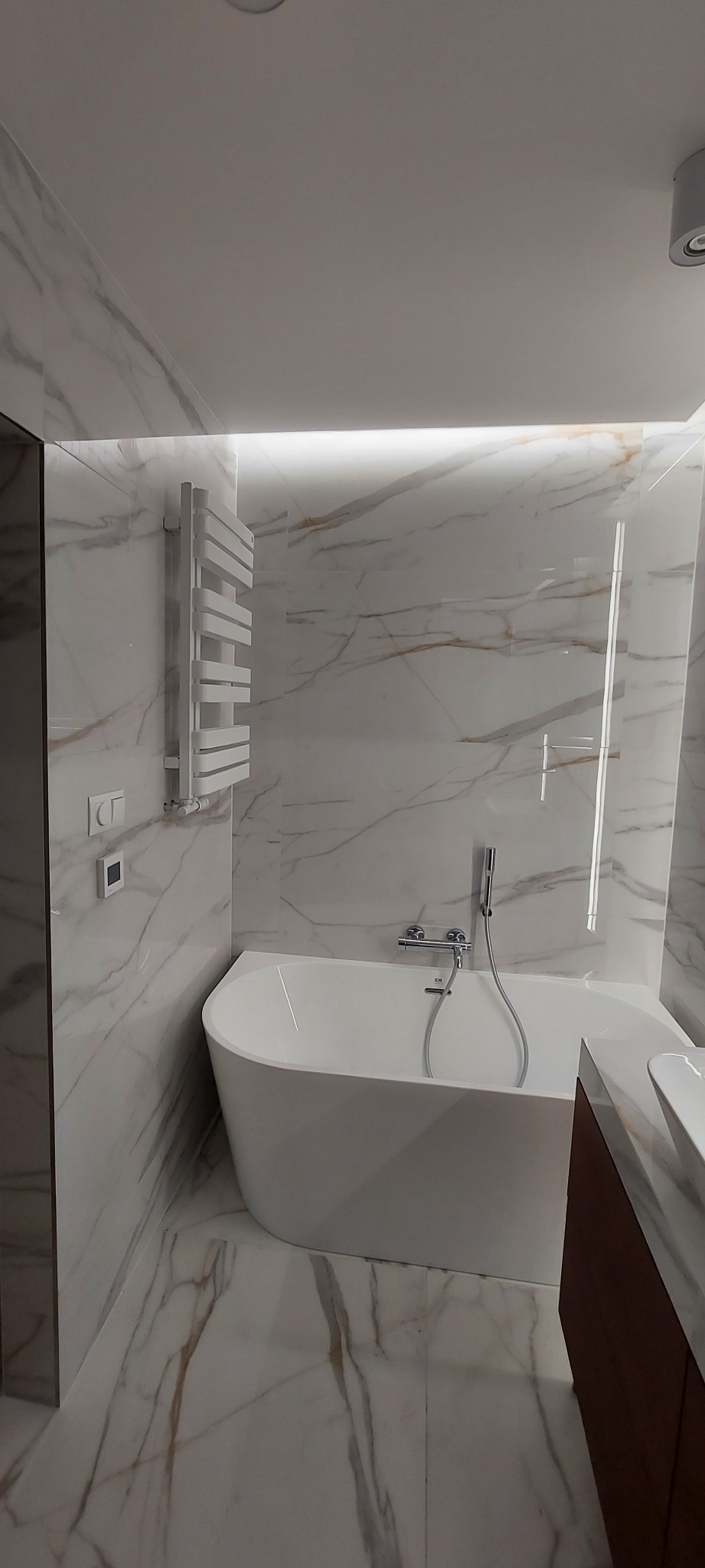 Nowoczesna łazienka we Wrocławiu z wanną wolnostojącą, grzejnikiem drabinkowym i marmurowymi płytkami, oświetlona subtelnym światłem LED.