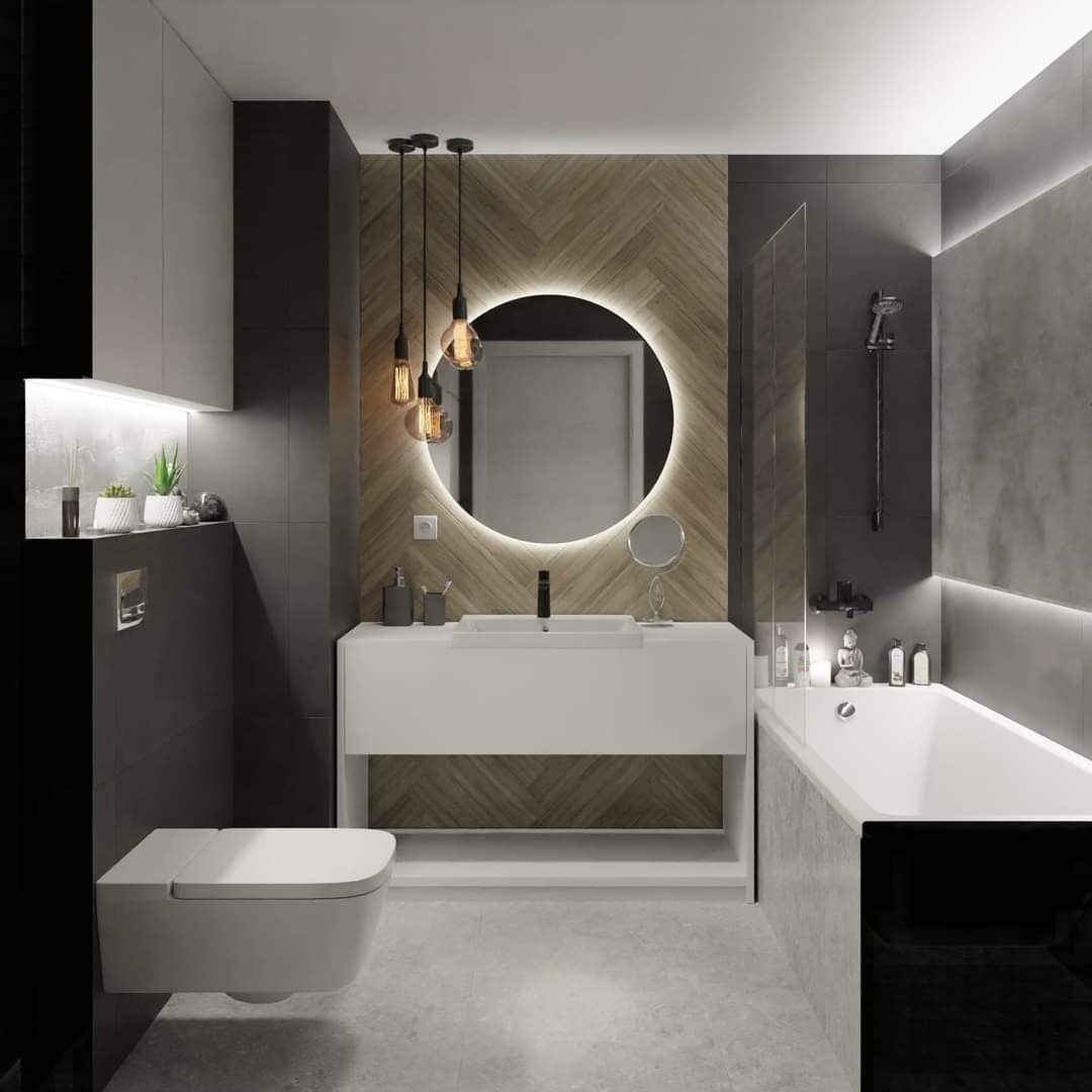 Nowoczesna łazienka z podświetlanym okrągłym lustrem, drewnianą ścianą w jodełkę, wiszącą toaletą i minimalistyczną białą szafką z umywalką.