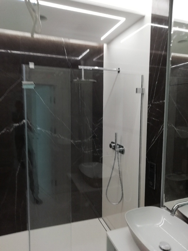 Nowoczesna kabina prysznicowa typu walk-in z deszczownicą, czarne marmurowe ściany, podświetlenie LED podsufitowe, biała umywalka nablatowa.