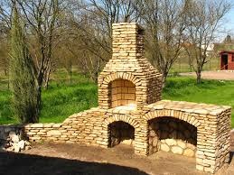 Ogród z murowanym grillem z kamienia naturalnego, z dodatkową przestrzenią roboczą i kominem, otoczony zielenią i drzewami.