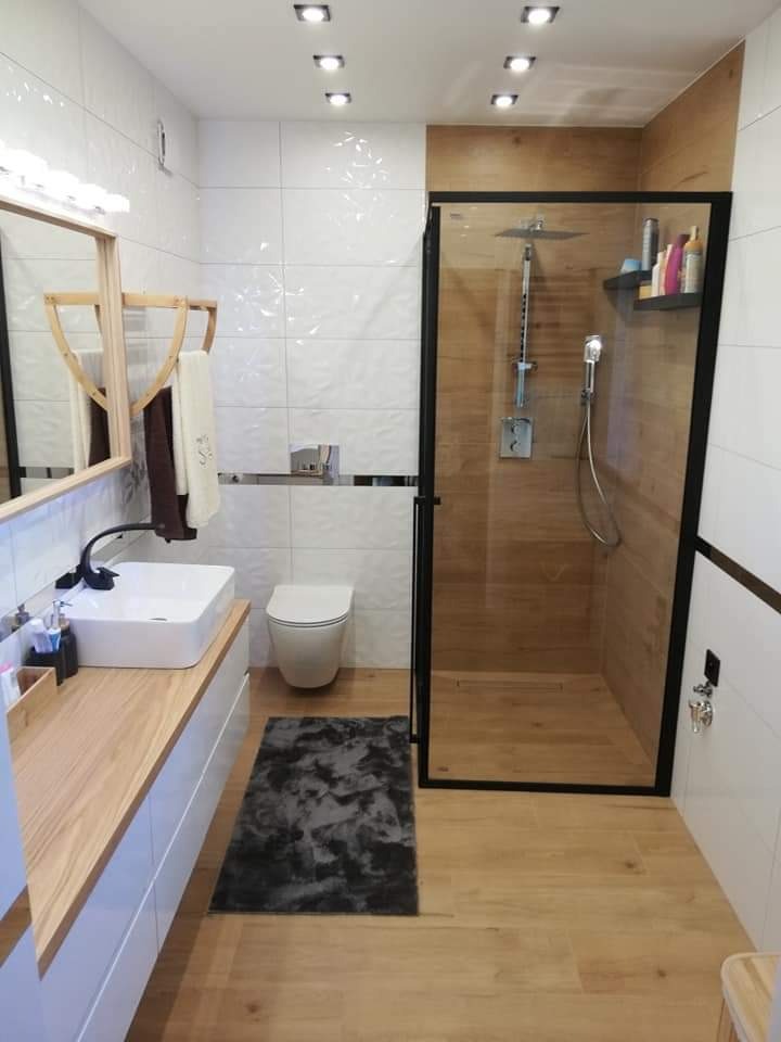 Nowoczesna łazienka z kabiną prysznicową typu walk-in, drewnopodobnymi płytkami, białymi płytkami strukturalnymi, umywalką nablatową na drewnianym blacie i szarą matą.