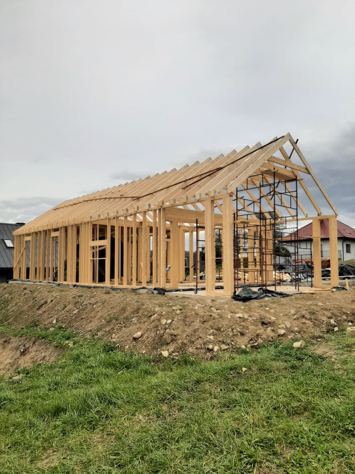 Konstrukcja domu szkieletowego w trakcie budowy w Michałowicach, widoczne drewniane ramy ścian i dachu, rusztowanie wewnątrz, teren nierówny.