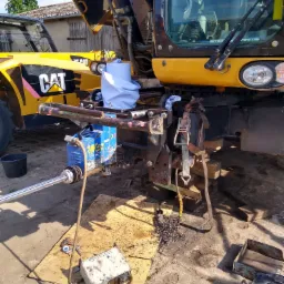 Żółta ładowarka teleskopowa CAT w trakcie naprawy, z podniesioną kabiną, widoczne narzędzia, metalowe wióry i hydrauliczny siłownik