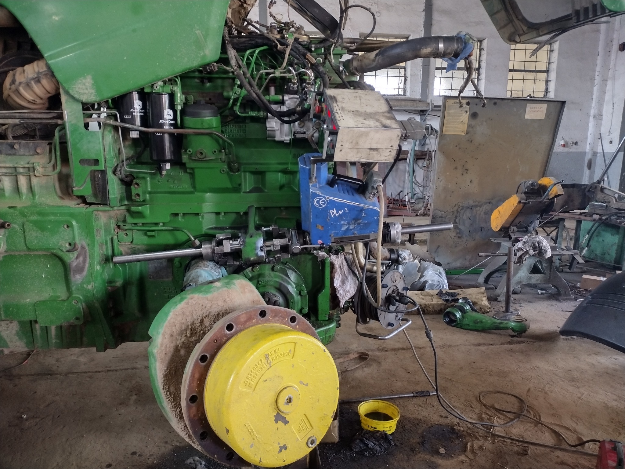 Zielony ciągnik John Deere w trakcie naprawy w warsztacie, widoczne filtry, silnik i żółta piasta koła