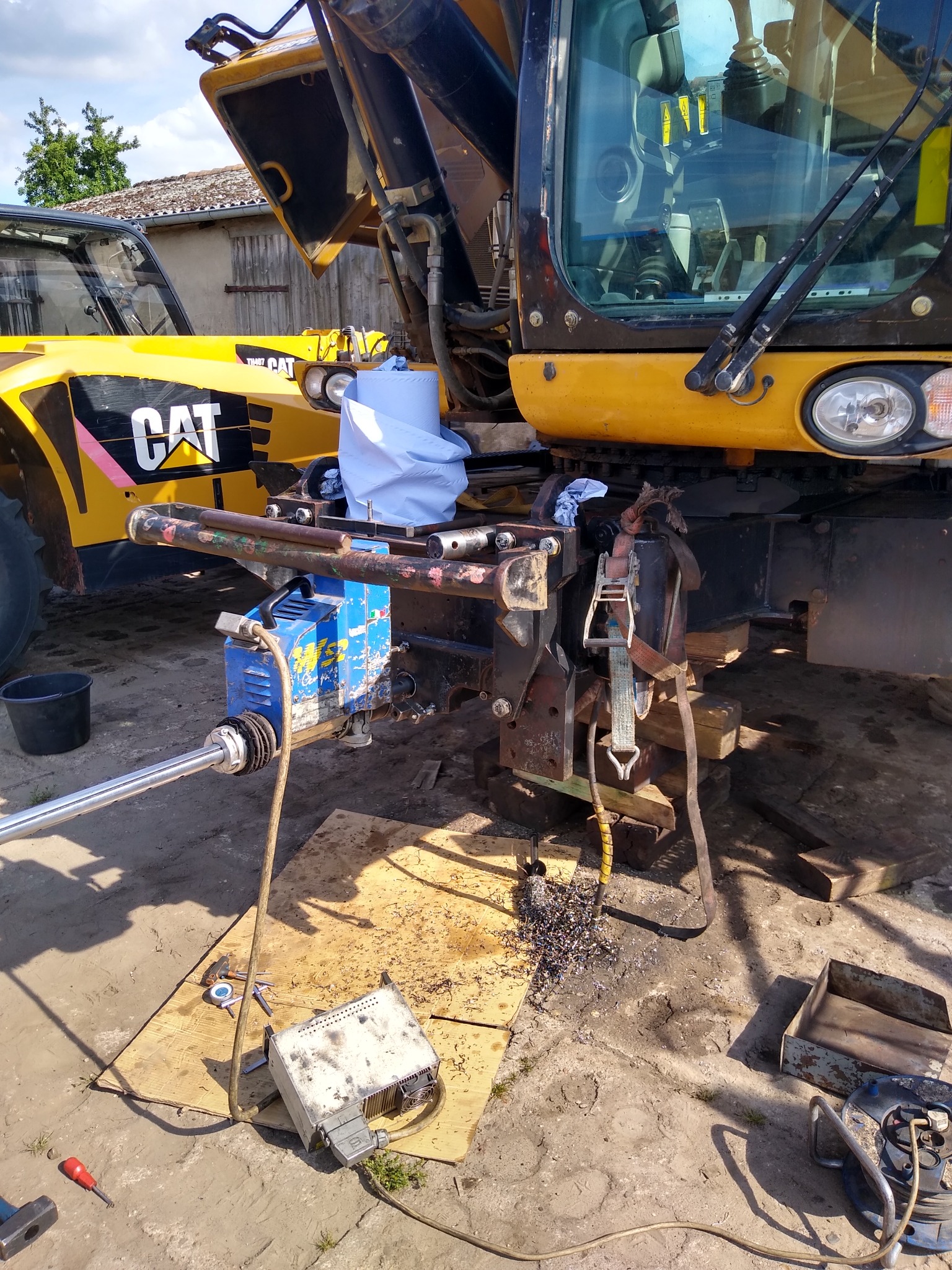 Żółta ładowarka teleskopowa CAT w trakcie naprawy, z podniesioną kabiną, widoczne narzędzia, metalowe wióry i hydrauliczny siłownik