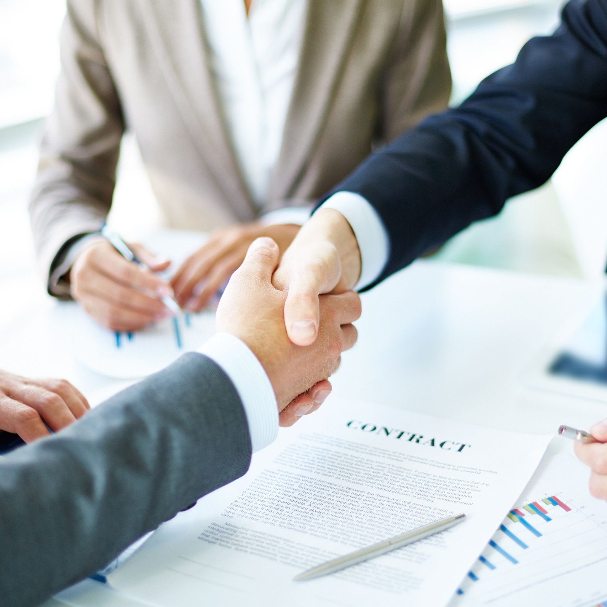Uścisk dłoni nad podpisanym kontraktem, widoczne wykresy i notatki, sugerujące pomyślne zakończenie negocjacji finansowych.