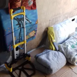 Wózek transportowy Stanley z rozkładaną platformą, narzędzia, pasy mocujące, koc i poduszki na kartonowym podłożu przygotowane do zabezpieczenia transportowanych przedmiotów.