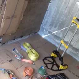 Wnętrze furgonetki z przygotowanymi narzędziami i akcesoriami do zabezpieczenia ładunku: wózek transportowy Stanley, pasy mocujące w różnych kolorach, komplet narzędzi i kartony ochronne.