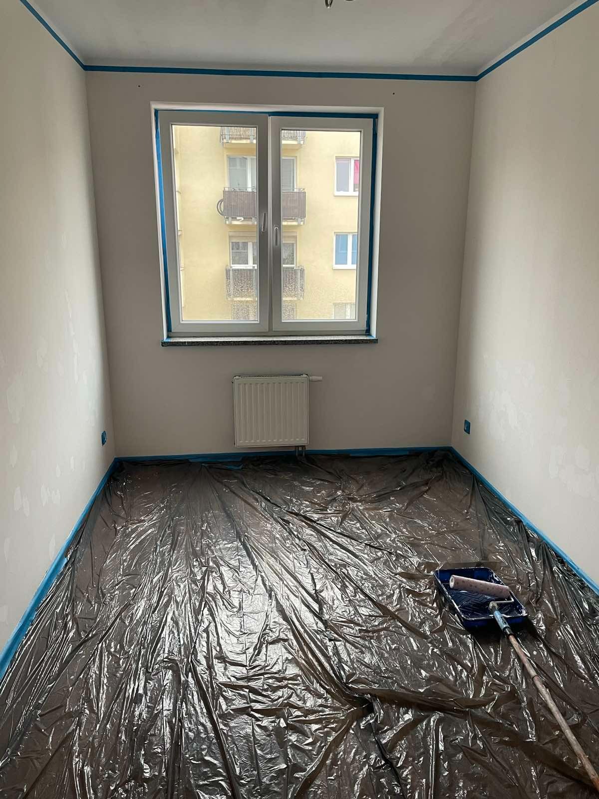 Pokój w Toruniu przygotowany do malowania: ściany częściowo zagruntowane, zabezpieczone folią i taśmą malarską, widoczny wałek i kuweta malarska.