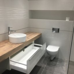 KuchnieNaWymiar - Nowoczesna łazienka z drewnianym blatem, okrągłą umywalką nablatową i otwartą szufladą pod blatem, minimalistyczna toaleta podwieszana.