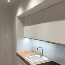 KuchnieNaWymiar - Nowoczesna, minimalistyczna kuchnia: białe, lakierowane fronty szafek, drewniany blat, biały zlew podwieszany i indukcyjna płyta grzewcza.