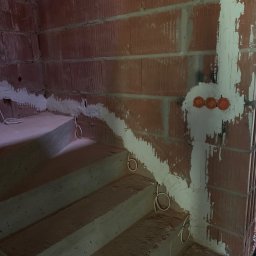 KliMal instalacje - Surowe schody betonowe w trakcie remontu z widoczną instalacją elektryczną w bruzdach wypełnionych gipsem oraz puszkami pod gniazdka w ścianie z pustaków ceramicznych.