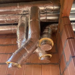 KliMal instalacje - System kanałów wentylacyjnych owiniętych folią aluminiową, zamontowanych pod sufitem z cegieł, widoczne izolacje z wełny mineralnej na końcach kanałów.
