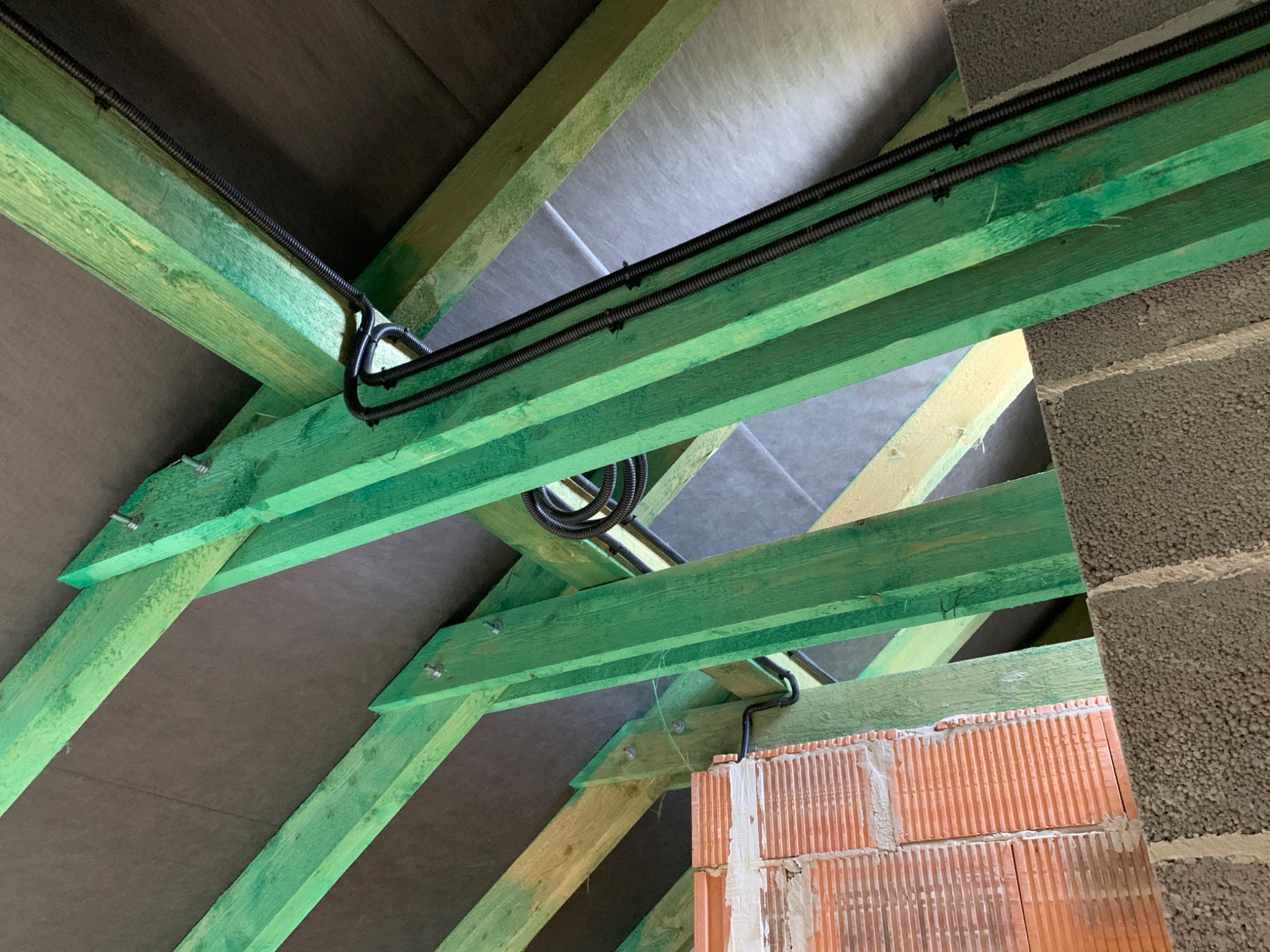 Instalacja elektryczna w peszlu, poprowadzona wzdłuż zielonych belek więźby dachowej, widok z dołu na poddaszu w trakcie budowy.