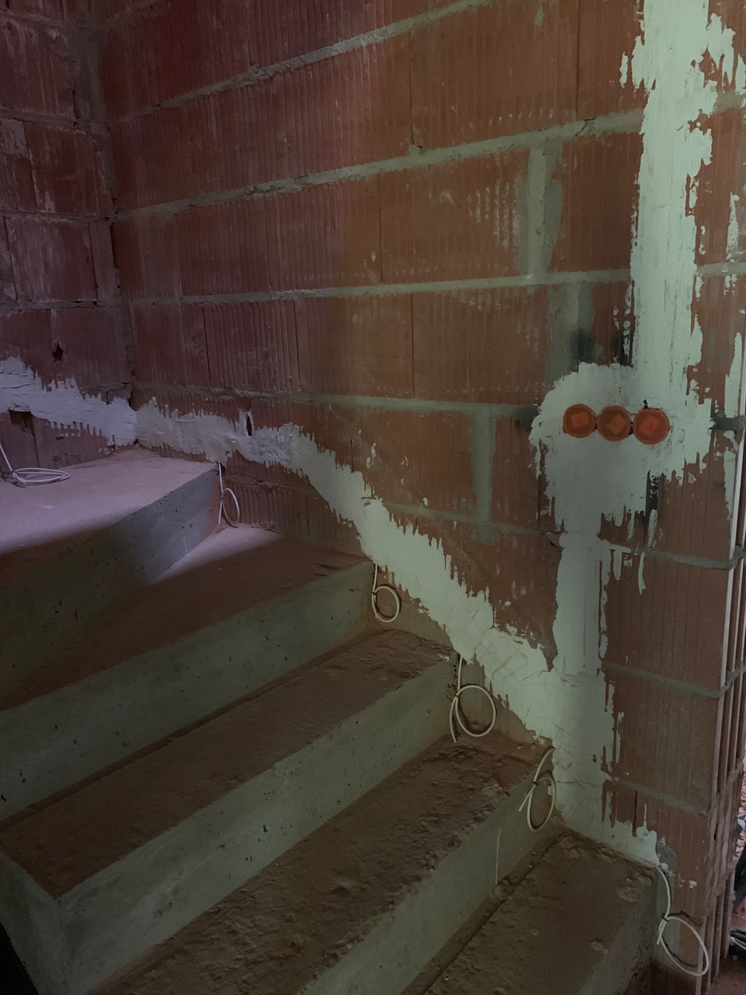 Surowe schody betonowe w trakcie remontu z widoczną instalacją elektryczną w bruzdach wypełnionych gipsem oraz puszkami pod gniazdka w ścianie z pustaków ceramicznych.