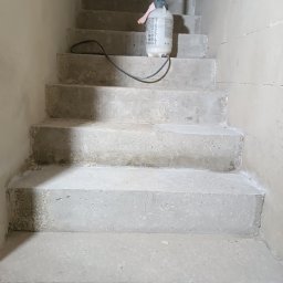 Krzysztof Rog - Betonowe schody w surowym stanie z rozpylaczem ciśnieniowym na górnym stopniu, widoczne niedoskonałości i porowatość betonu.