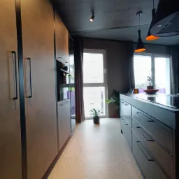 Nowoczesna kuchnia z szarą zabudową, jasną posadzką lastryko i oświetleniem punktowym, widok z perspektywy podłogi.