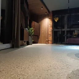 Jasna, szlifowana podłoga z terazzo w nowoczesnym salonie z ceglaną ścianą, drewnianymi elementami i rośliną doniczkową.