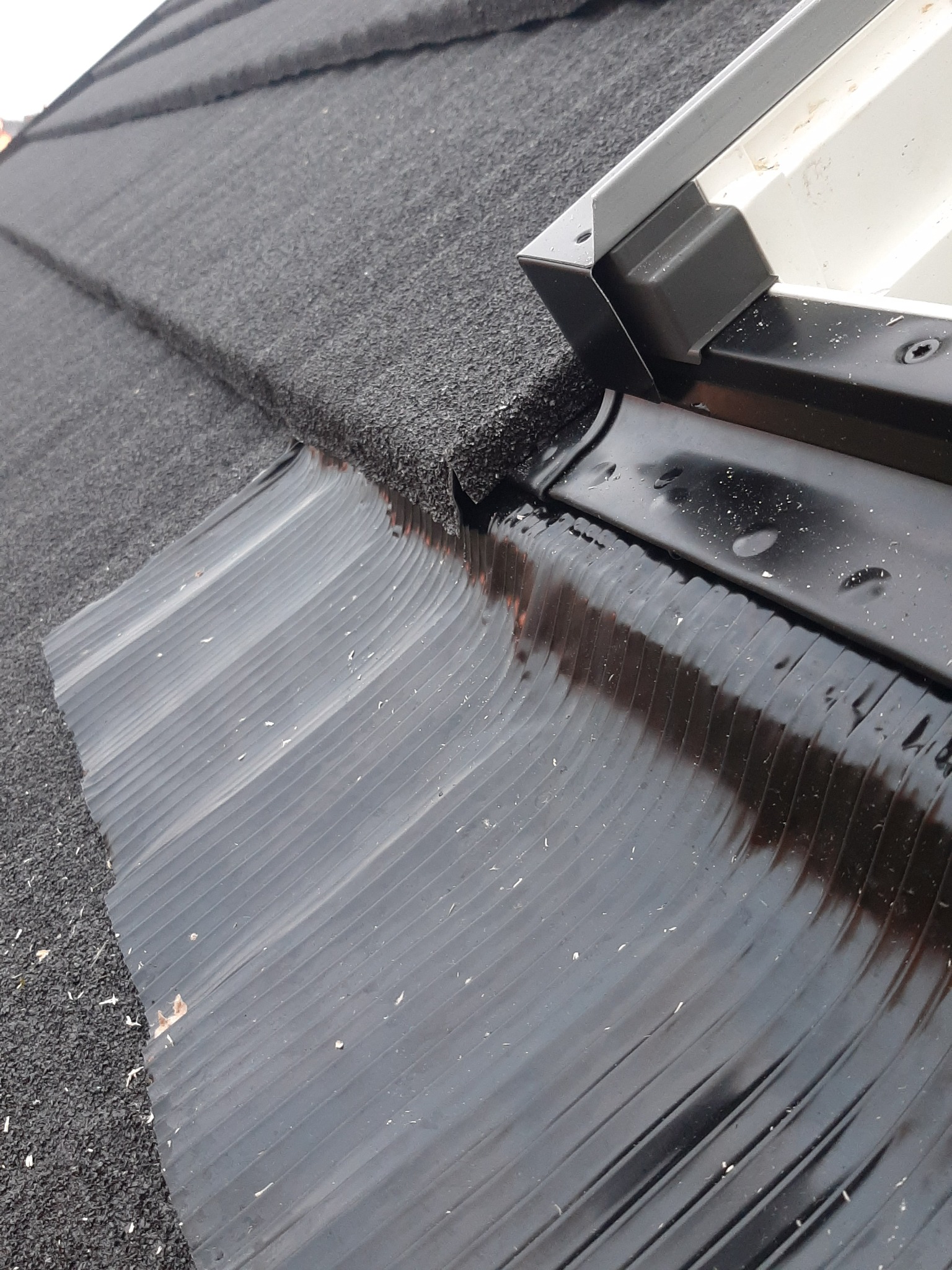 Fragment dachu pokrytego szarą papą z widocznym fragmentem rynny i obróbki blacharskiej.