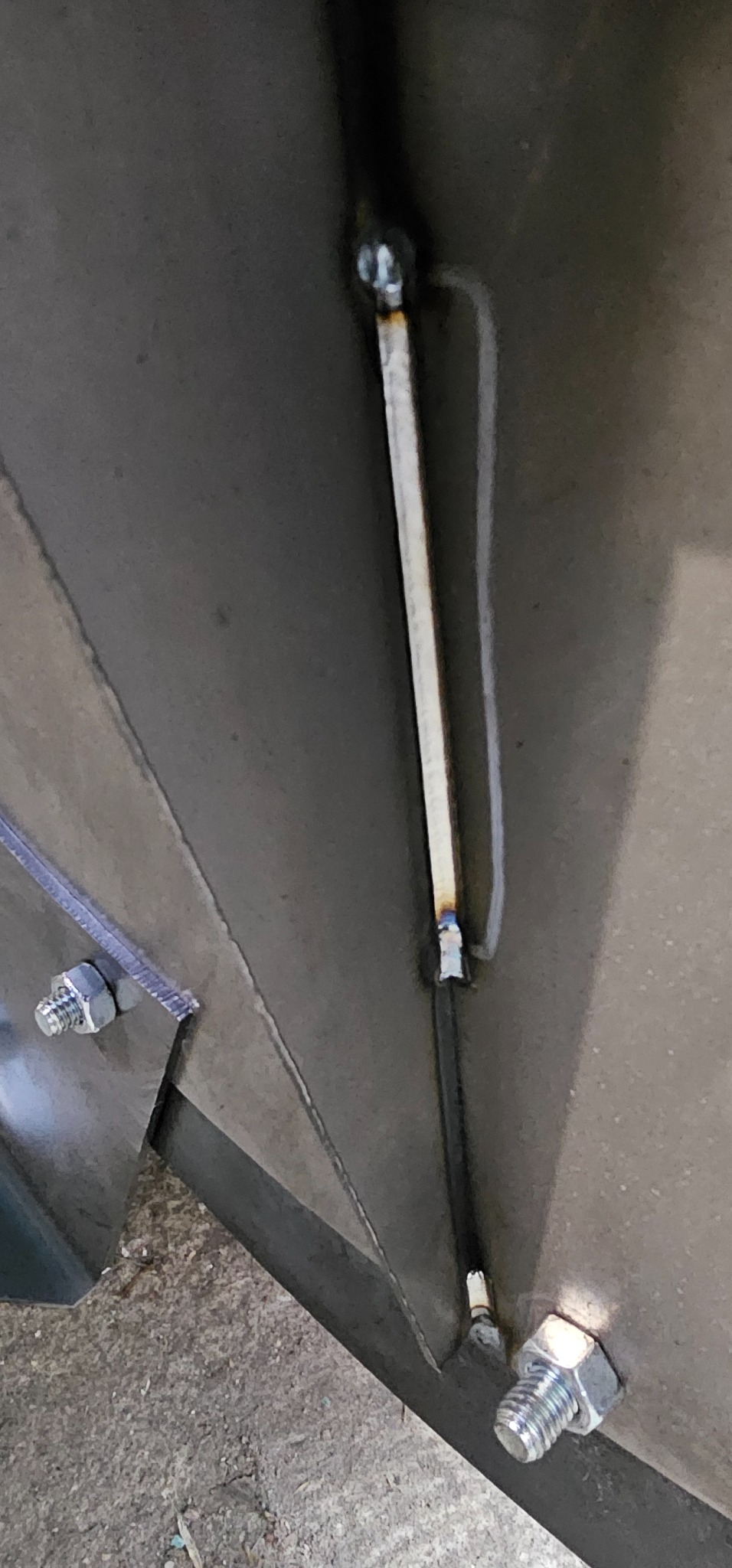 Detal spawania metalowej konstrukcji, widoczne spawy, śruby mocujące oraz fragment podłoża.