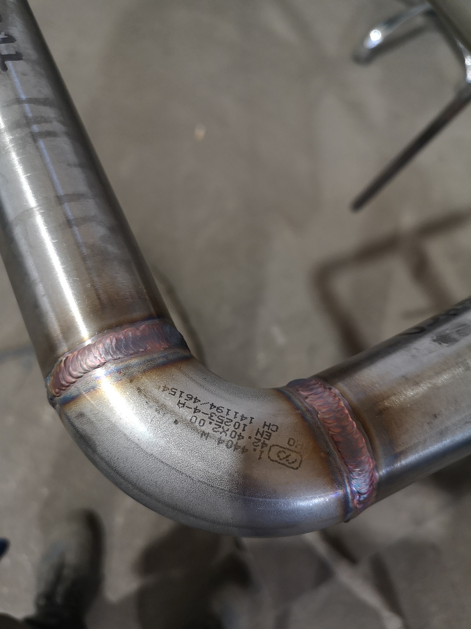 Metalowa rura z precyzyjnym spoinem kątowym, widoczne oznaczenia techniczne na powierzchni rury.