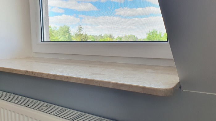 Zamontowane okno z marmurowym parapetem w domu w Zielonce, widok na błękitne niebo i zieleń drzew za oknem.