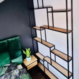 Ręcznie robiony regał Loft z czarną metalową ramą i drewnianymi półkami, wykonany w Łęcznej, ustawiony w sypialni z zielonymi akcentami.