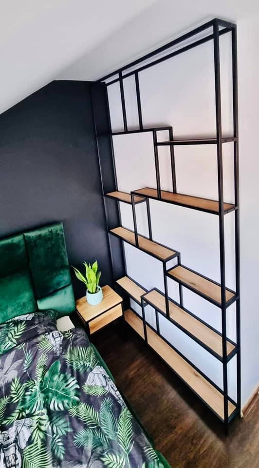 Ręcznie robiony regał Loft z czarną metalową ramą i drewnianymi półkami, wykonany w Łęcznej, ustawiony w sypialni z zielonymi akcentami.