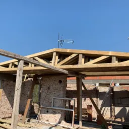 Budowa dachu domu w trakcie realizacji: drewniana konstrukcja więźby dachowej, murowane ściany z cegły dziurawki, niebieskie niebo w tle.