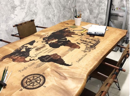 Drewniany stół z nieregularnymi krawędziami, zdobiony mapą świata i kompasem, otoczony krzesłami z płóciennymi oparciami.