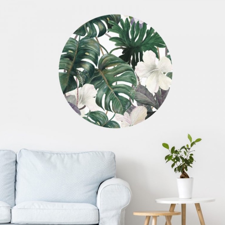 Naklejka ścienna z motywem tropikalnych liści i białych kwiatów hibiskusa w okrągłej ramie, umieszczona nad jasnoniebieską sofą w minimalistycznym wnętrzu.