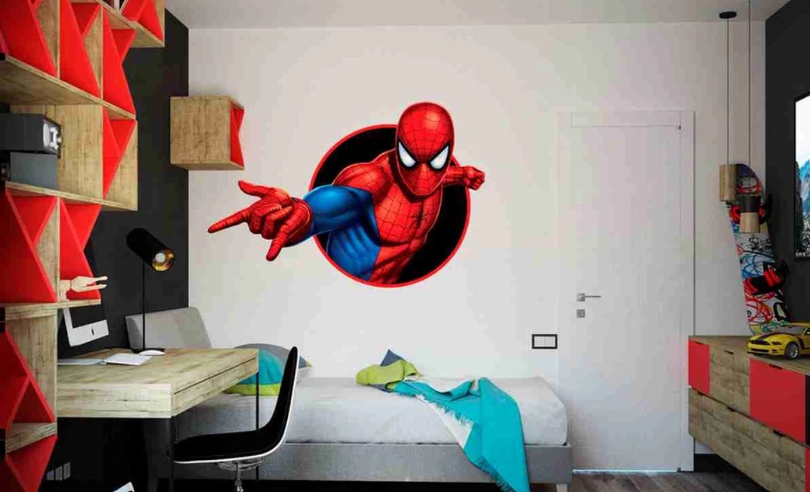 Pokój dziecięcy z naklejką ścienną przedstawiającą Spider-Mana wychodzącego ze ściany, biurko z lampką i łóżko z turkusowym pledem.