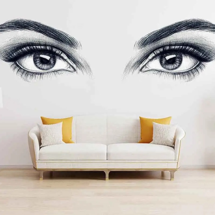 Ręcznie rysowane oczy nad białą sofą z żółtymi poduszkami na białej ścianie, tworzące artystyczną dekorację wnętrza.