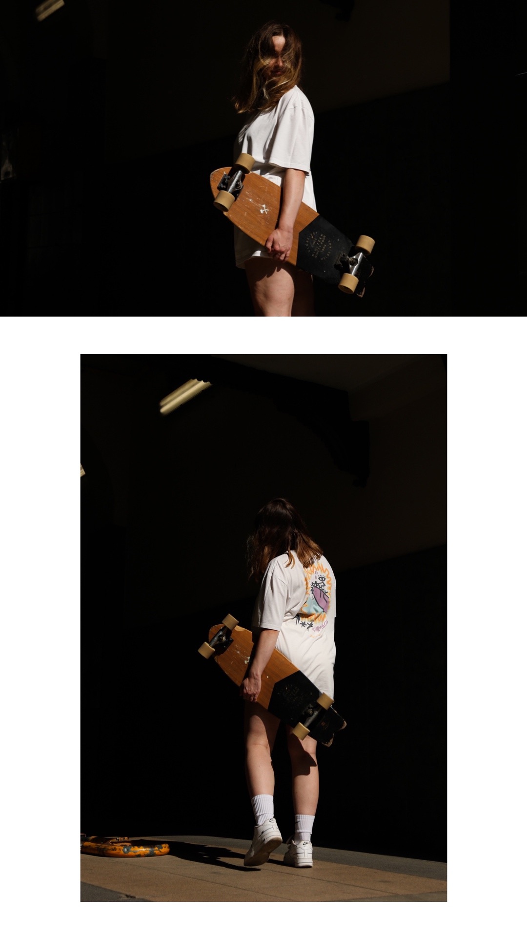 Kobieta w białej koszulce z nadrukiem na plecach trzyma drewnianą deskorolkę longboard w zacienionym otoczeniu.