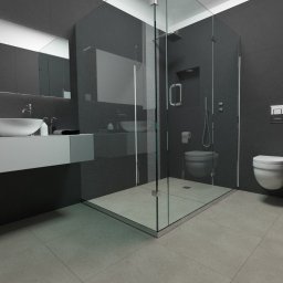 PSV-SERVICE SP.z.o.o - Nowoczesna łazienka w odcieniach szarości z kabiną prysznicową typu walk-in, wiszącą toaletą i umywalką nablatową na szafce. Widoczny minimalistyczny design i duże, ciemne płytki na ścianach.